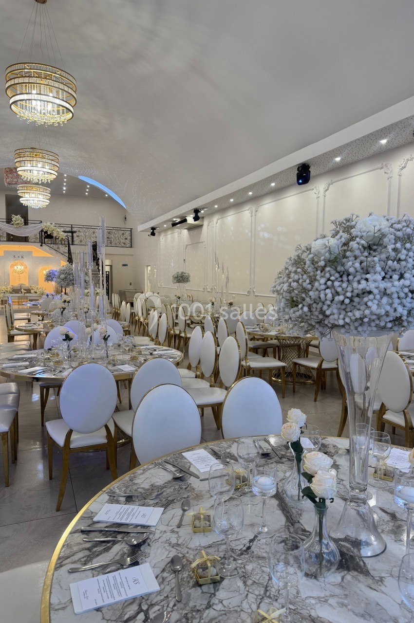 Salle de réception élégante avec tables rondes décorées de fleurs blanches et lustres suspendus.