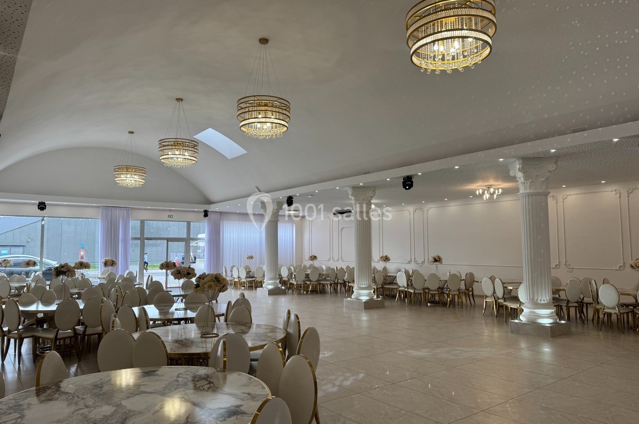 Salle de réception lumineuse avec tables rondes, chaises blanches et dorées, colonnes blanches et lustres élégants.
