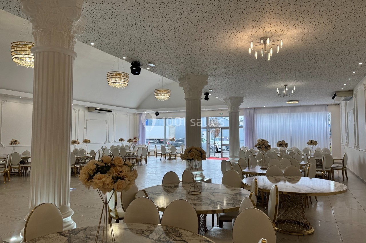 Salle de réception lumineuse avec tables rondes en marbre, chaises blanches et colonnes décoratives.