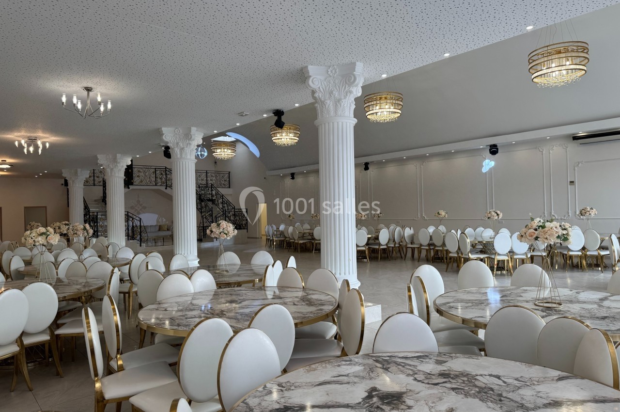 Salle de réception lumineuse avec tables rondes en marbre, chaises blanches et colonnes décoratives blanches.