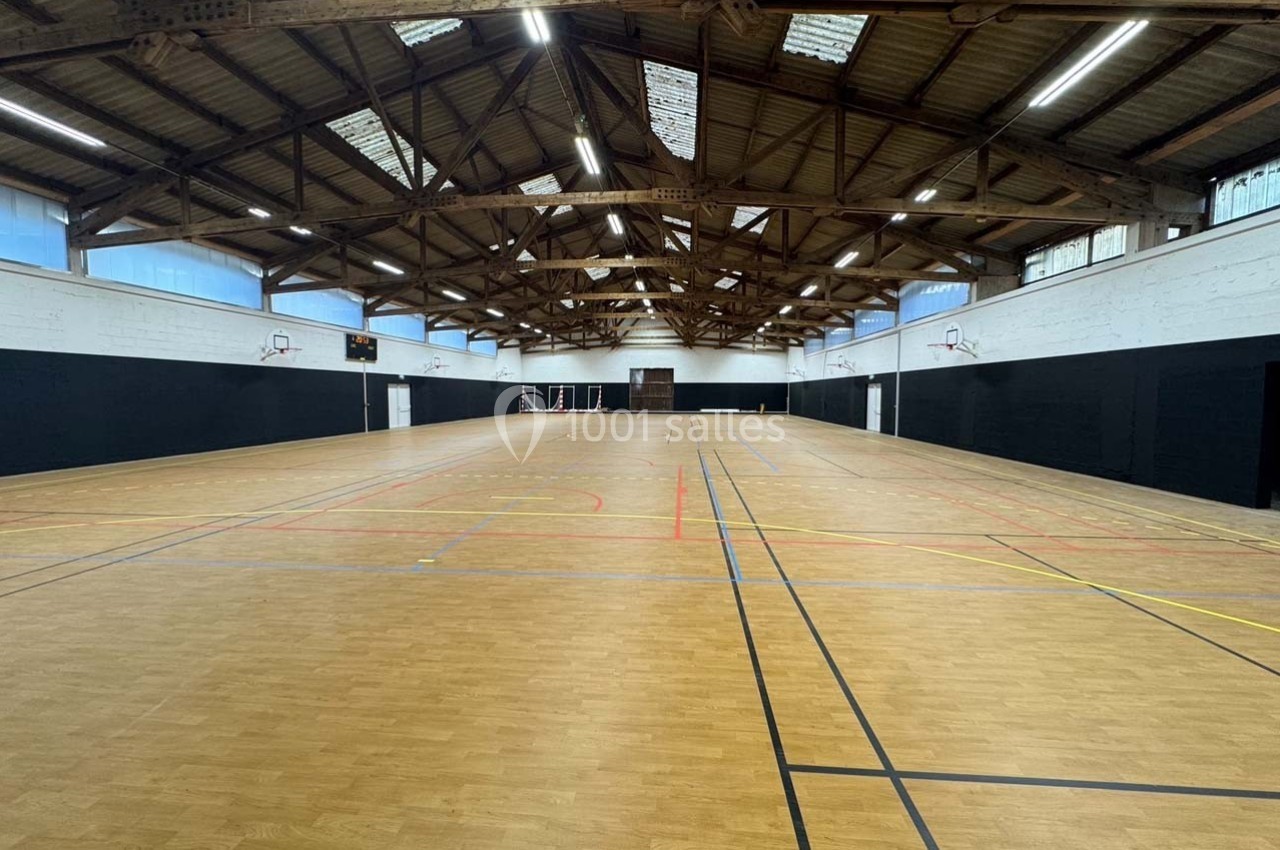 Salle de sport intérieure avec parquet, lignes de marquage au sol et paniers de basketball fixés aux murs.