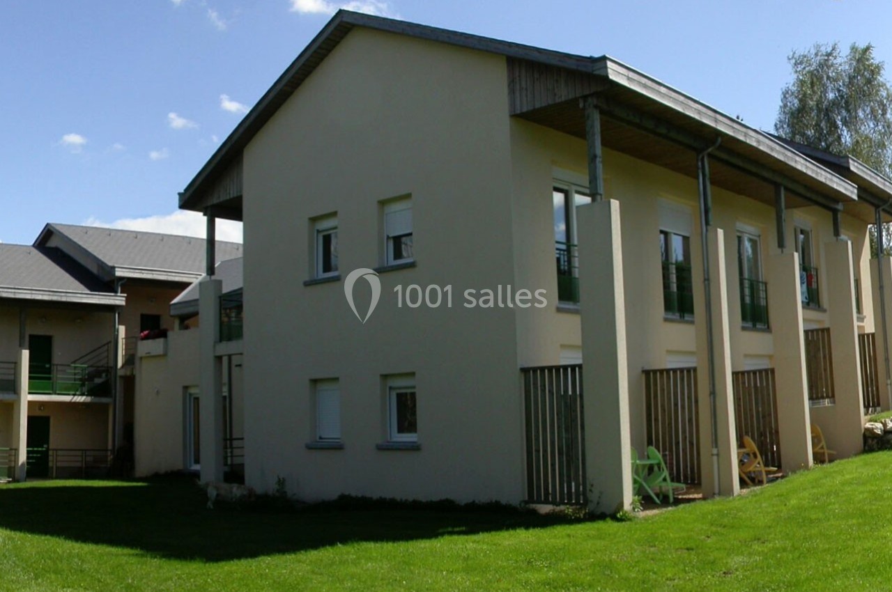 Bâtiment résidentiel moderne à deux étages avec jardin et chaises colorées sur une pelouse.