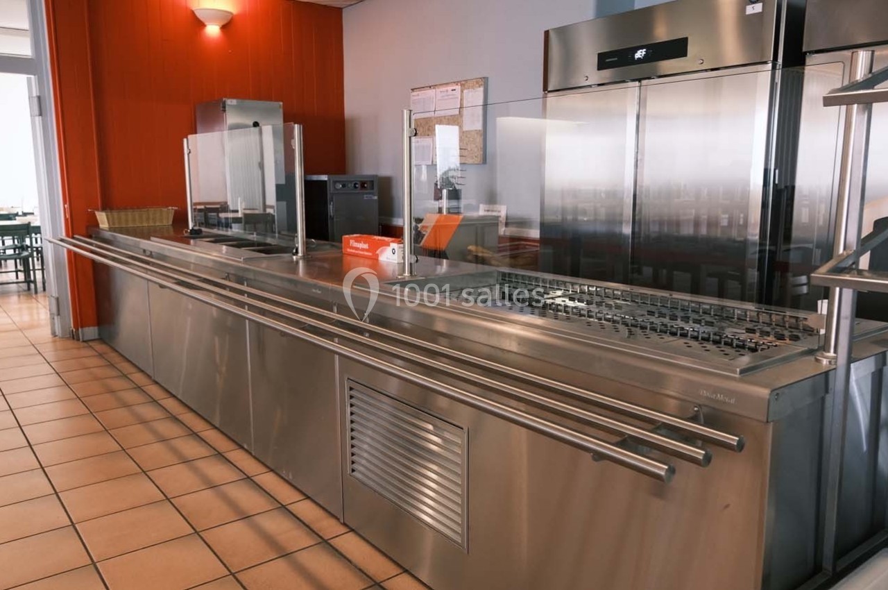 Comptoir de self-service en inox dans une cantine avec équipements de cuisine et réfrigérateurs en arrière-plan.