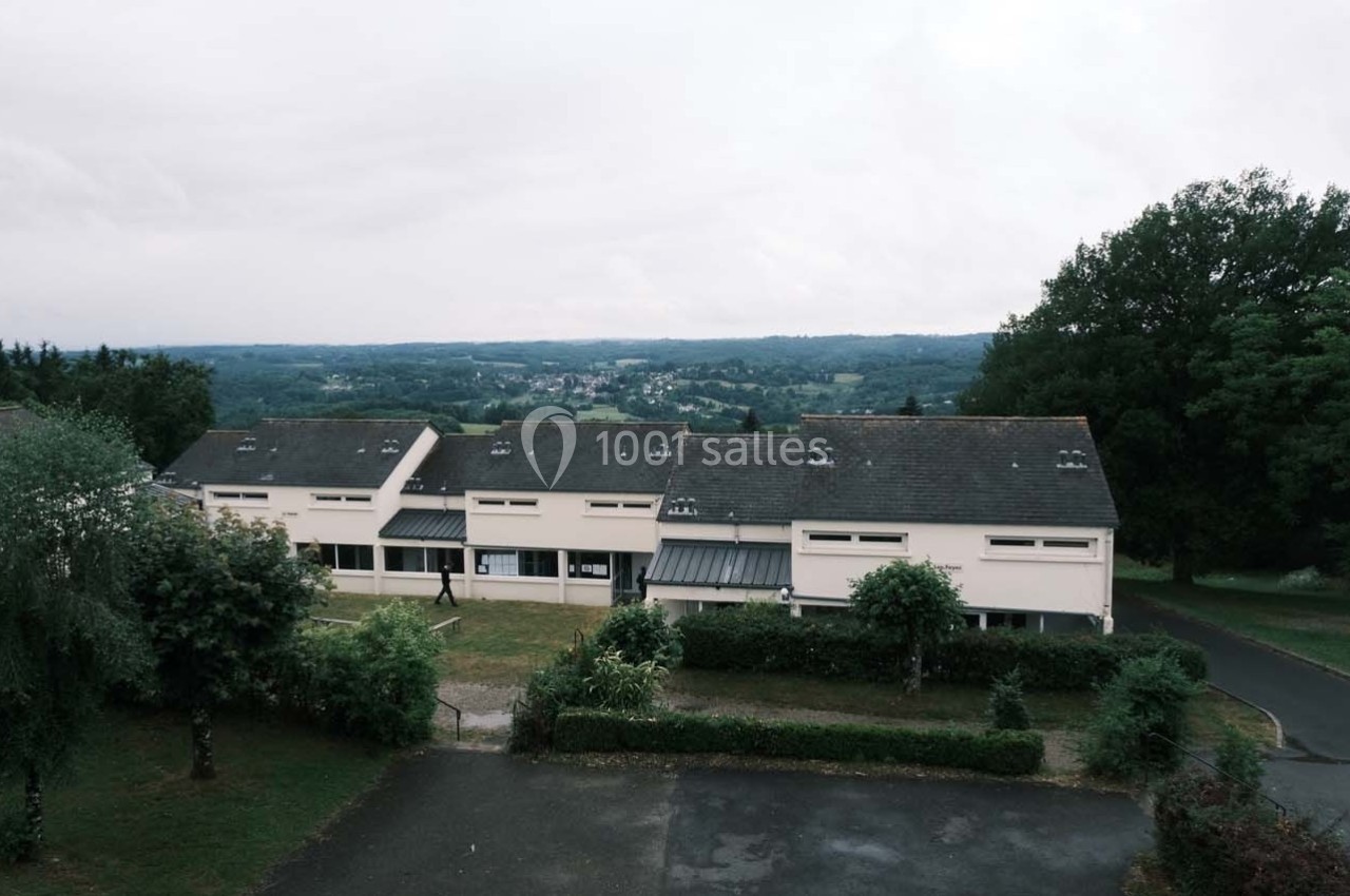 Vue aérienne de bâtiments résidentiels entourés de verdure, avec un paysage vallonné en arrière-plan.