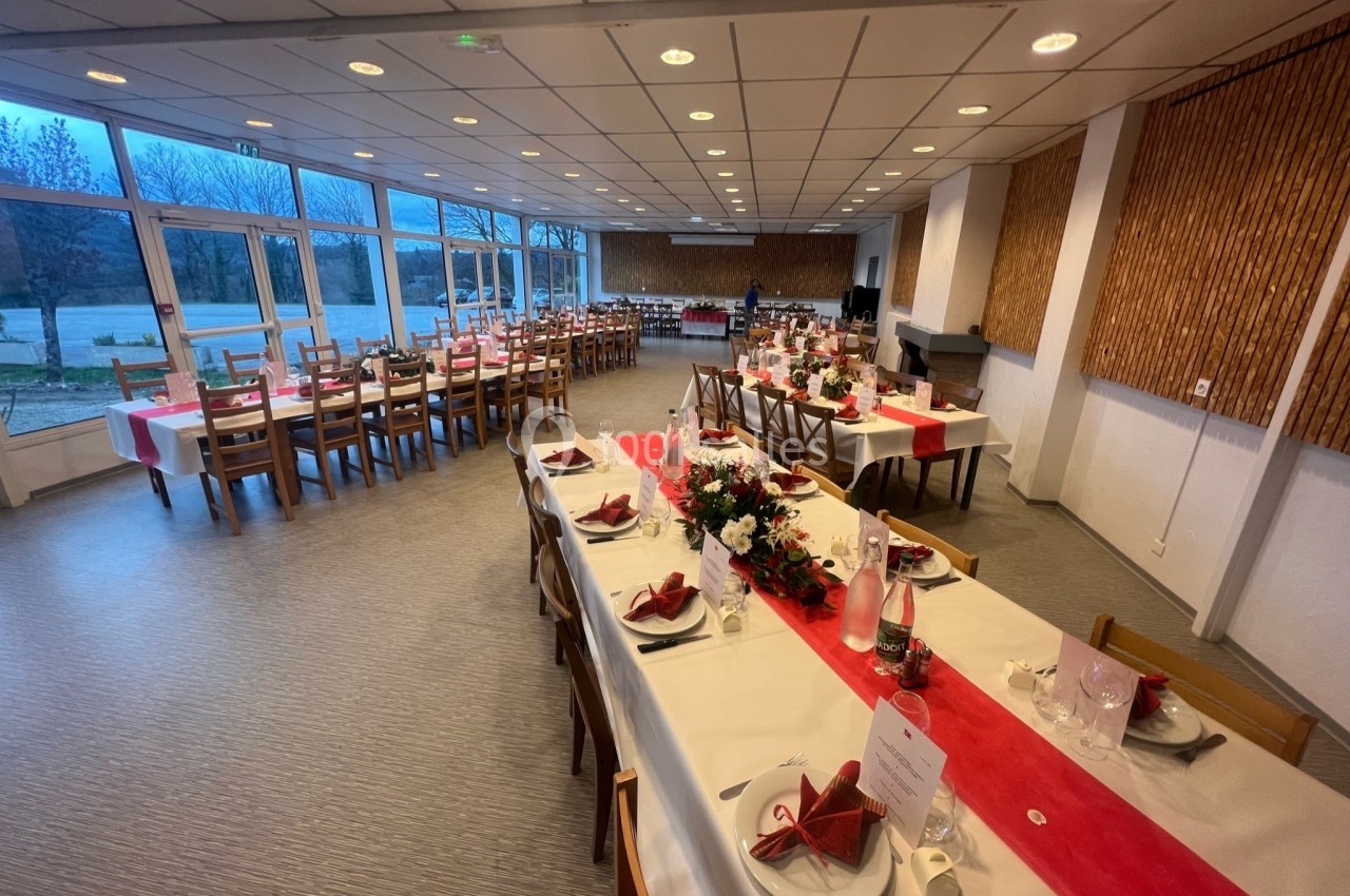 Salle de réception décorée avec des tables dressées, nappes blanches et rouges, et arrangements floraux.