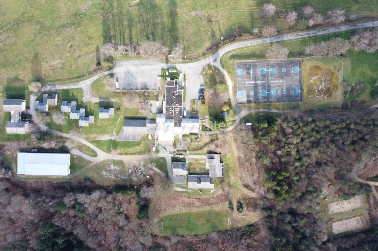 Vue aérienne d'un complexe comprenant des bâtiments, un terrain de sport et des espaces verts environnants.
