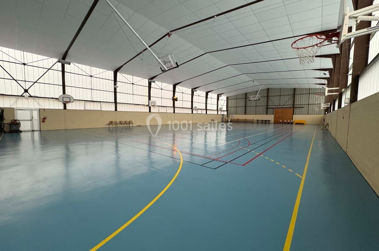 Salle de sport intérieure avec sol bleu, paniers de basket et lignes de marquage pour différentes activités.