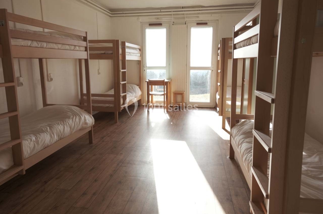 Dortoir lumineux avec lits superposés en bois, parquet au sol et une table près des fenêtres.