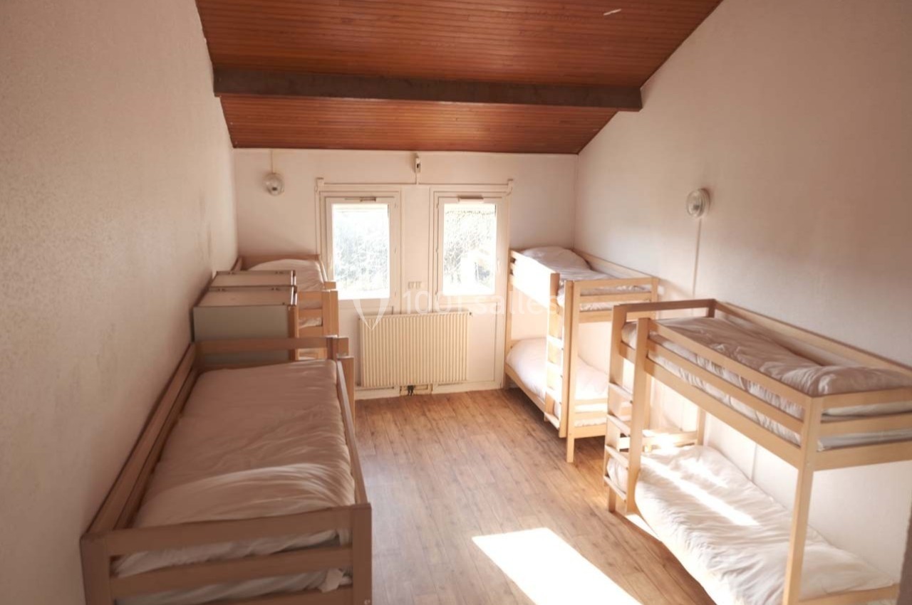 Dortoir lumineux avec lits superposés en bois, parquet au sol et plafond en bois incliné.
