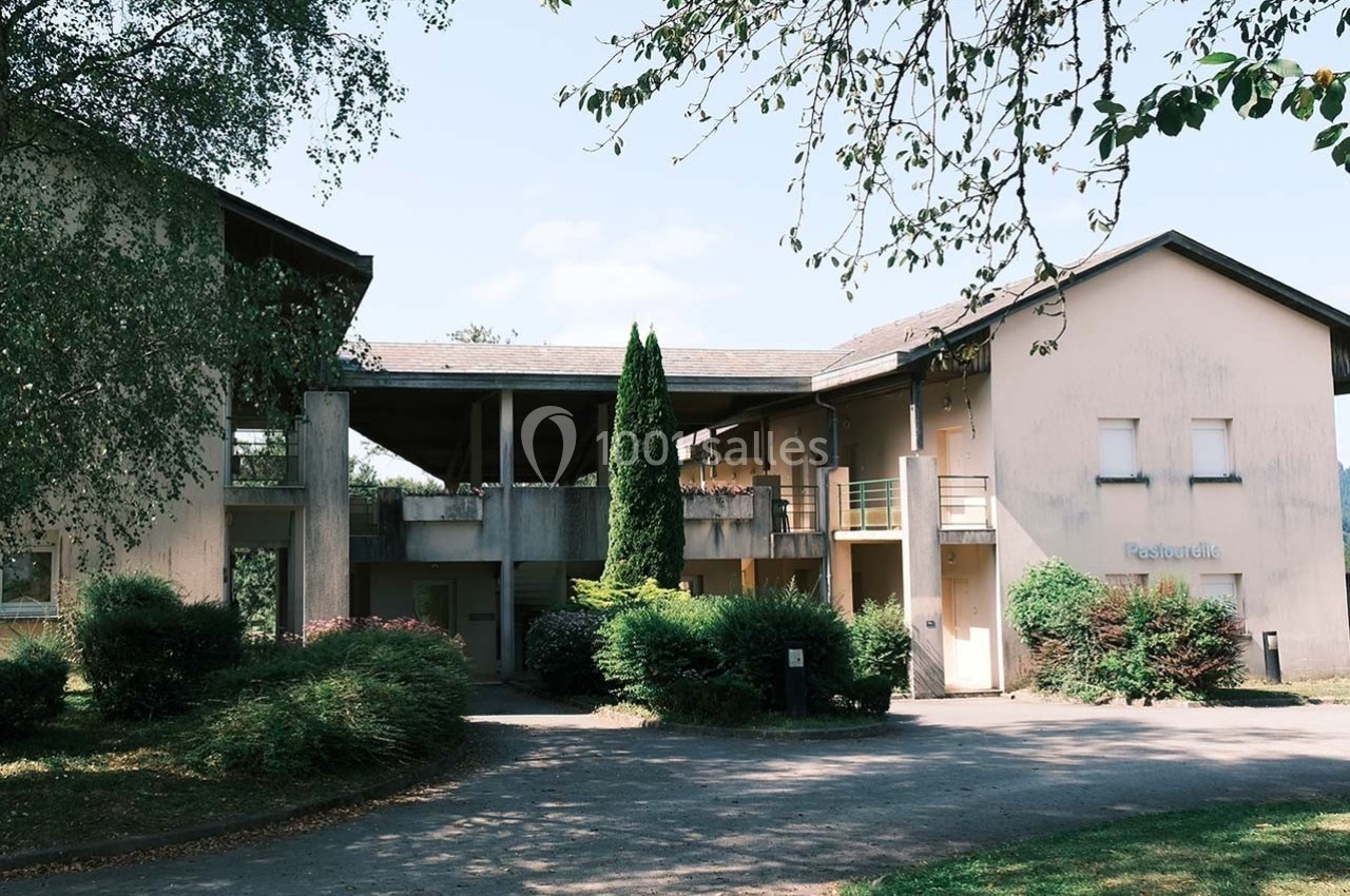 Bâtiment résidentiel beige entouré de végétation, avec un chemin d'accès et un arbre au premier plan.