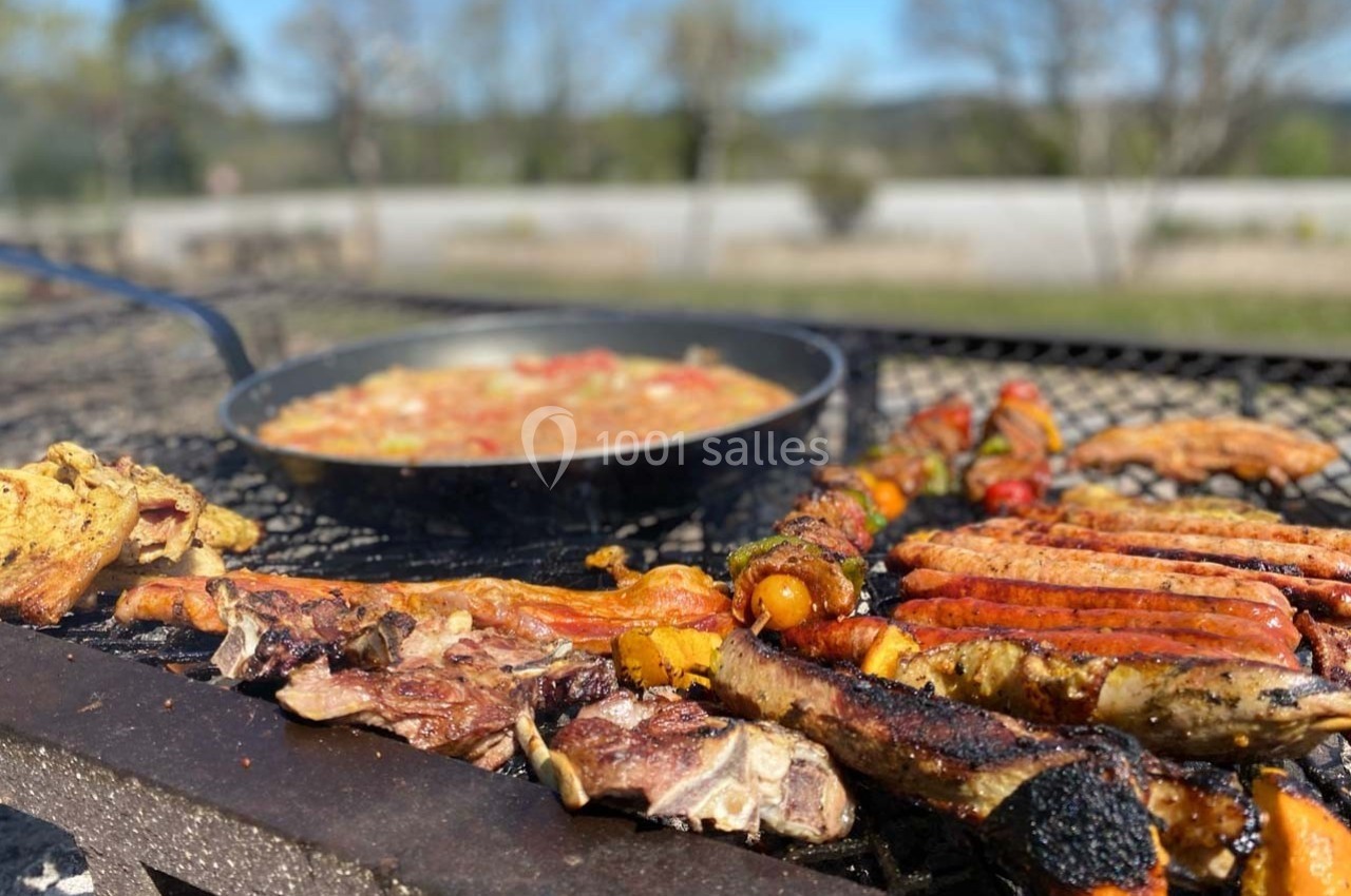 Viande grillée et légumes sur un barbecue, avec une poêle de plat mijoté en arrière-plan dans un cadre extérieur.