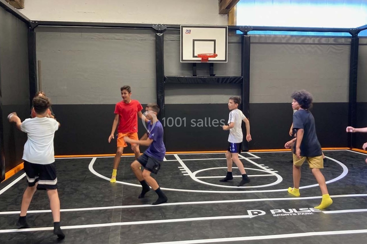 Des enfants jouent au basket dans un gymnase intérieur avec un terrain délimité et un panier mural.
