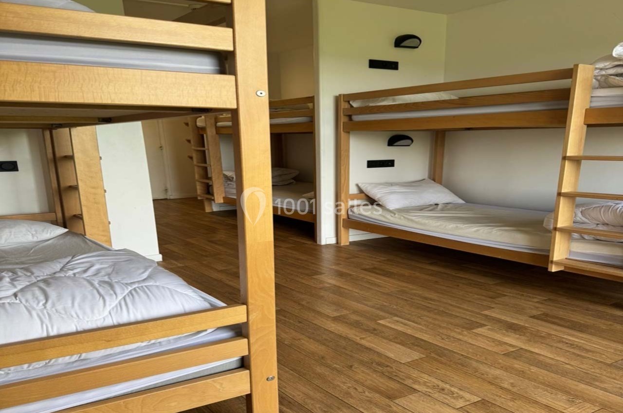 Dortoir avec lits superposés en bois, matelas et oreillers blancs, sol en parquet clair.