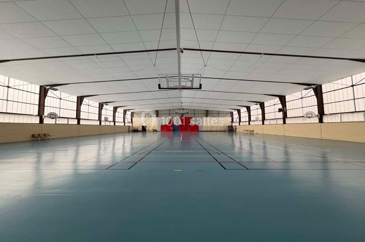 Salle de sport intérieure avec terrain de basket, sol bleu et panneaux de basket fixés aux murs.