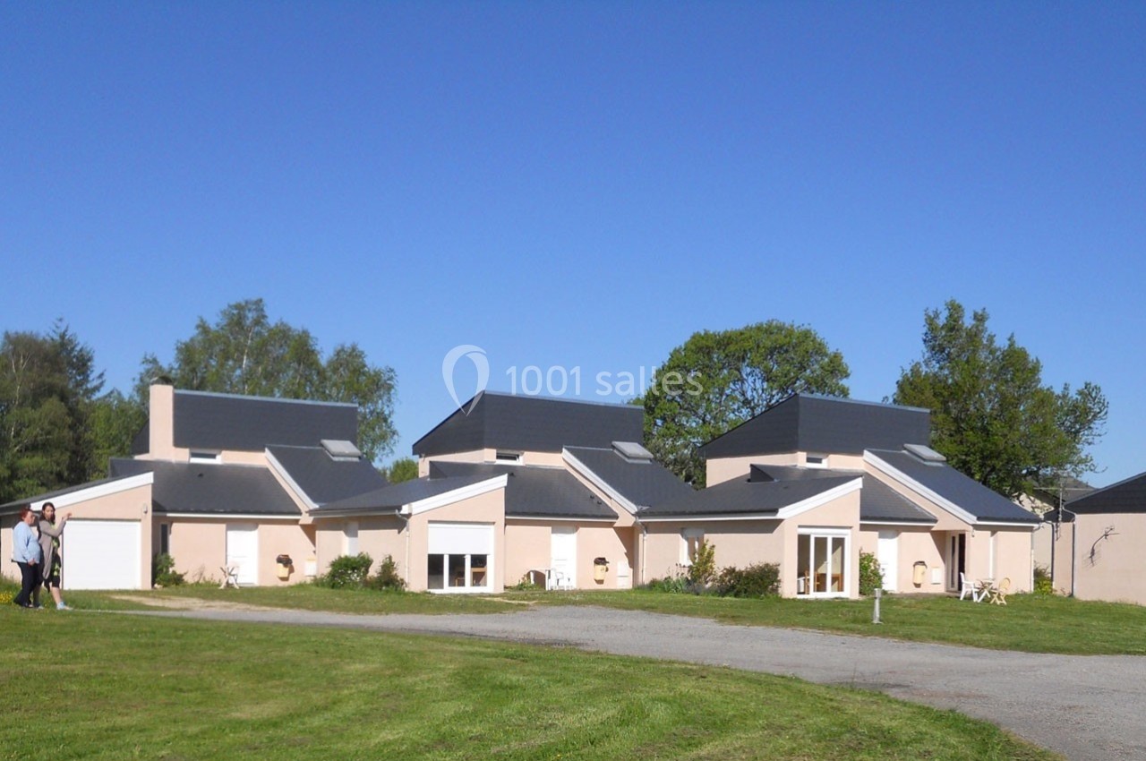 Maisons modernes avec toits en pente, entourées de pelouses et d'arbres, sous un ciel bleu dégagé.