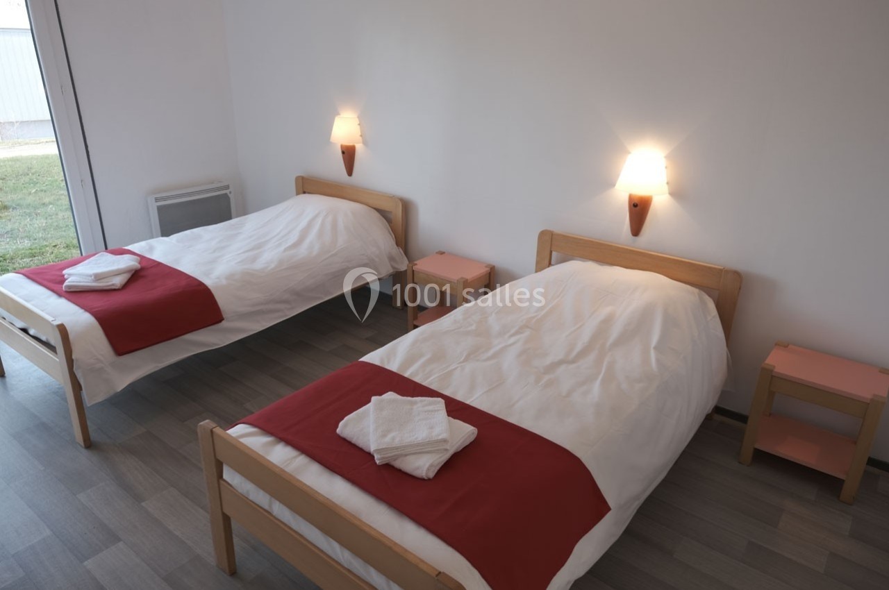 Deux lits simples avec draps blancs et chemins de lit rouges dans une chambre lumineuse au sol en parquet.