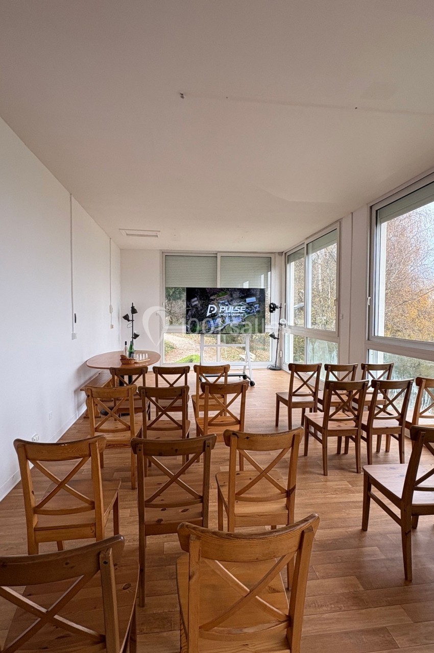 Salle lumineuse avec parquet, équipée de chaises en bois disposées face à un écran de présentation.