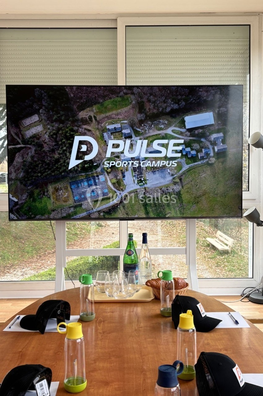 Vue d'une salle avec une table dressée et un écran affichant ’Pulse Sports Campus’ devant une fenêtre.