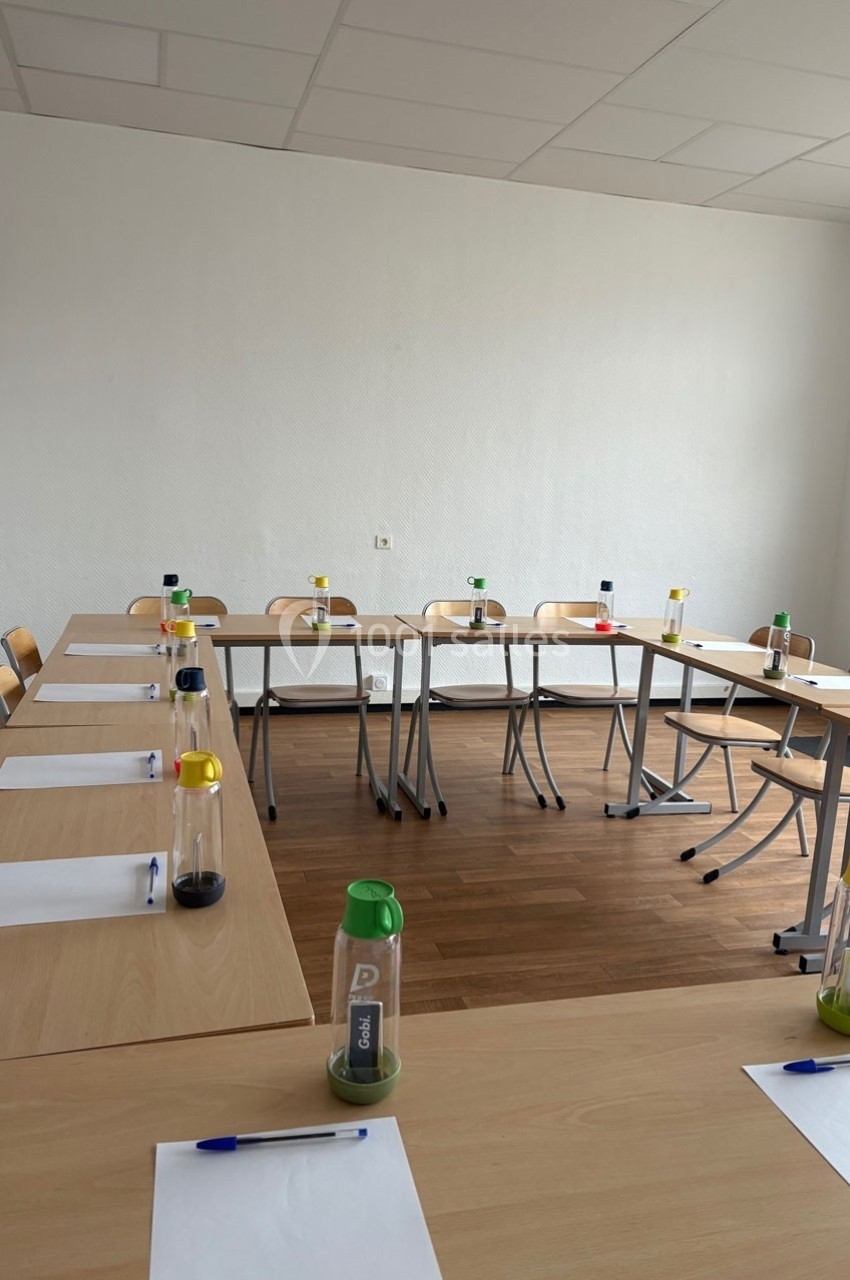 Salle de réunion avec tables disposées en U, chaises, bouteilles d'eau, feuilles et stylos prêts pour une session.