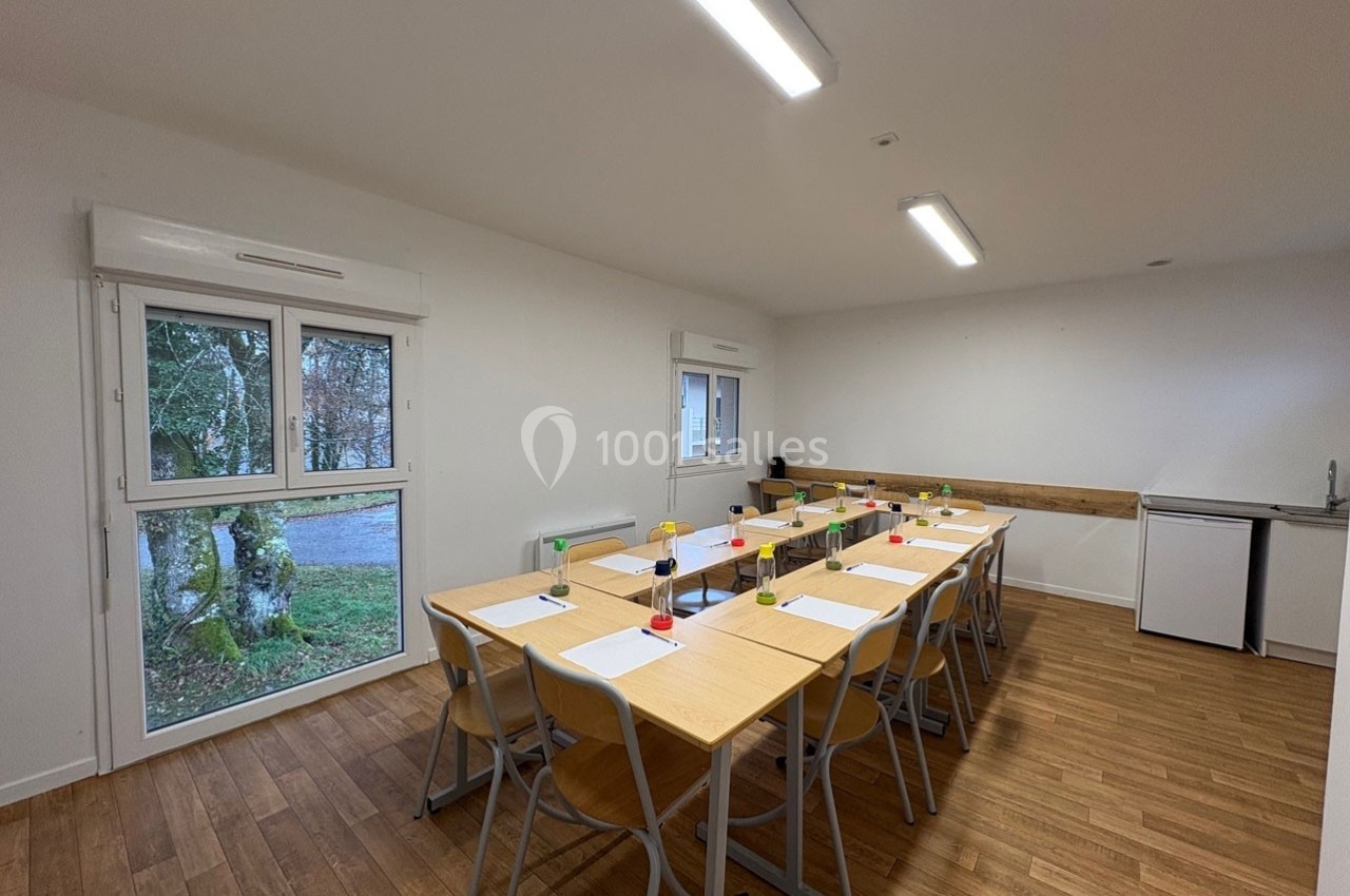 Salle de réunion lumineuse avec tables en bois, chaises, documents, stylos et vue sur l'extérieur par de grandes fenêtres.