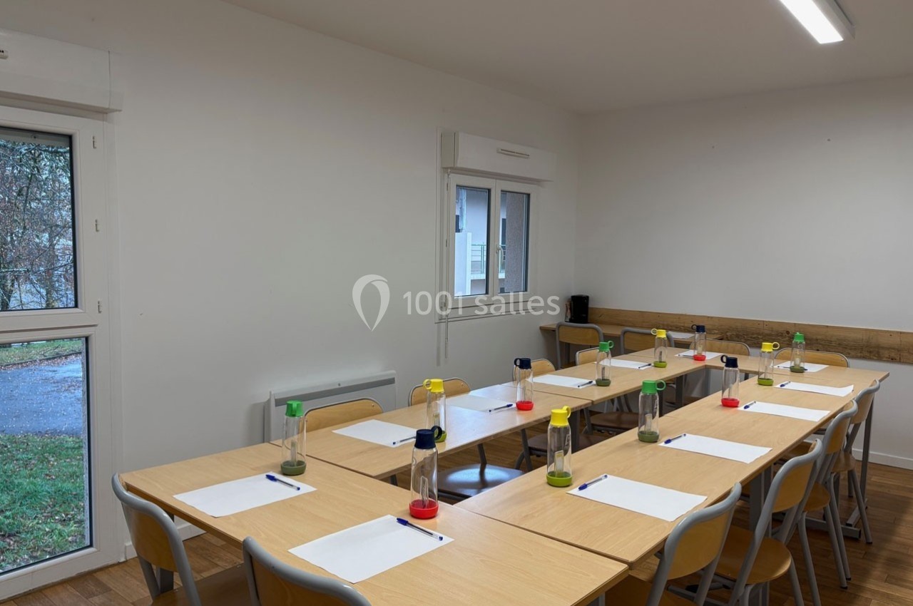 Salle de réunion lumineuse avec une grande table en bois, des chaises et des fournitures disposées pour une activité.