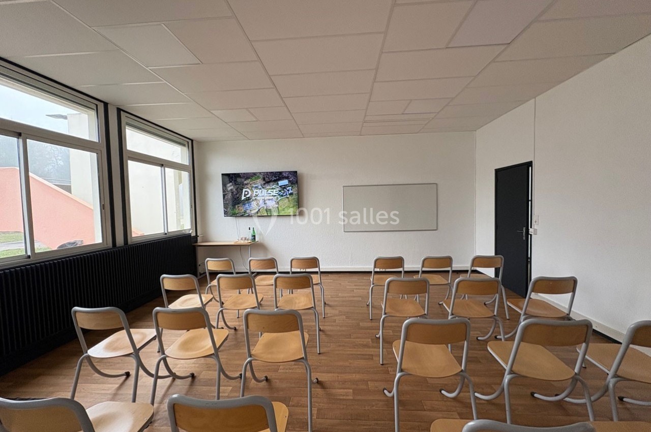 Salle de réunion vide avec des chaises alignées, un écran allumé au fond et un tableau blanc sur le mur.