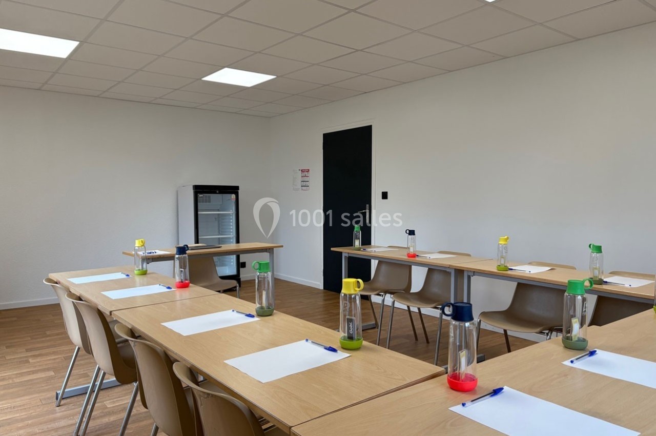Salle de réunion lumineuse avec des tables disposées en U, des chaises, des bouteilles d'eau et des blocs-notes.
