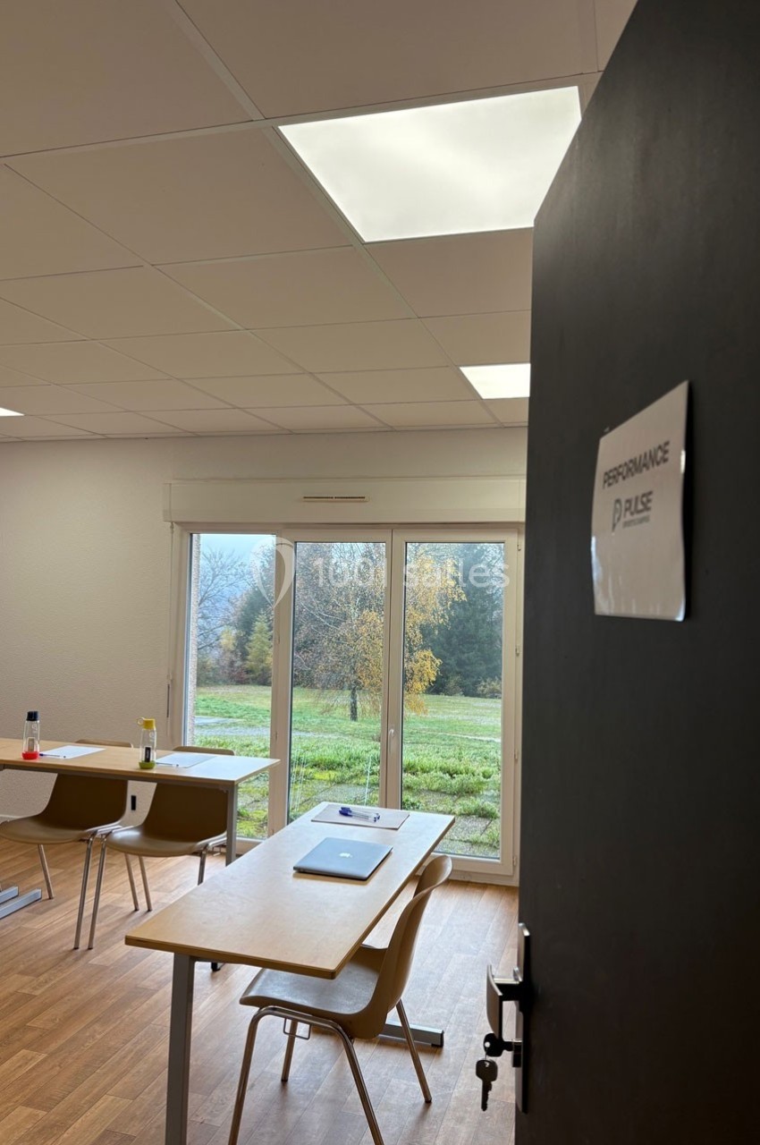 Salle de formation lumineuse avec des tables, des chaises et une vue sur un extérieur arboré à travers de grandes baies…