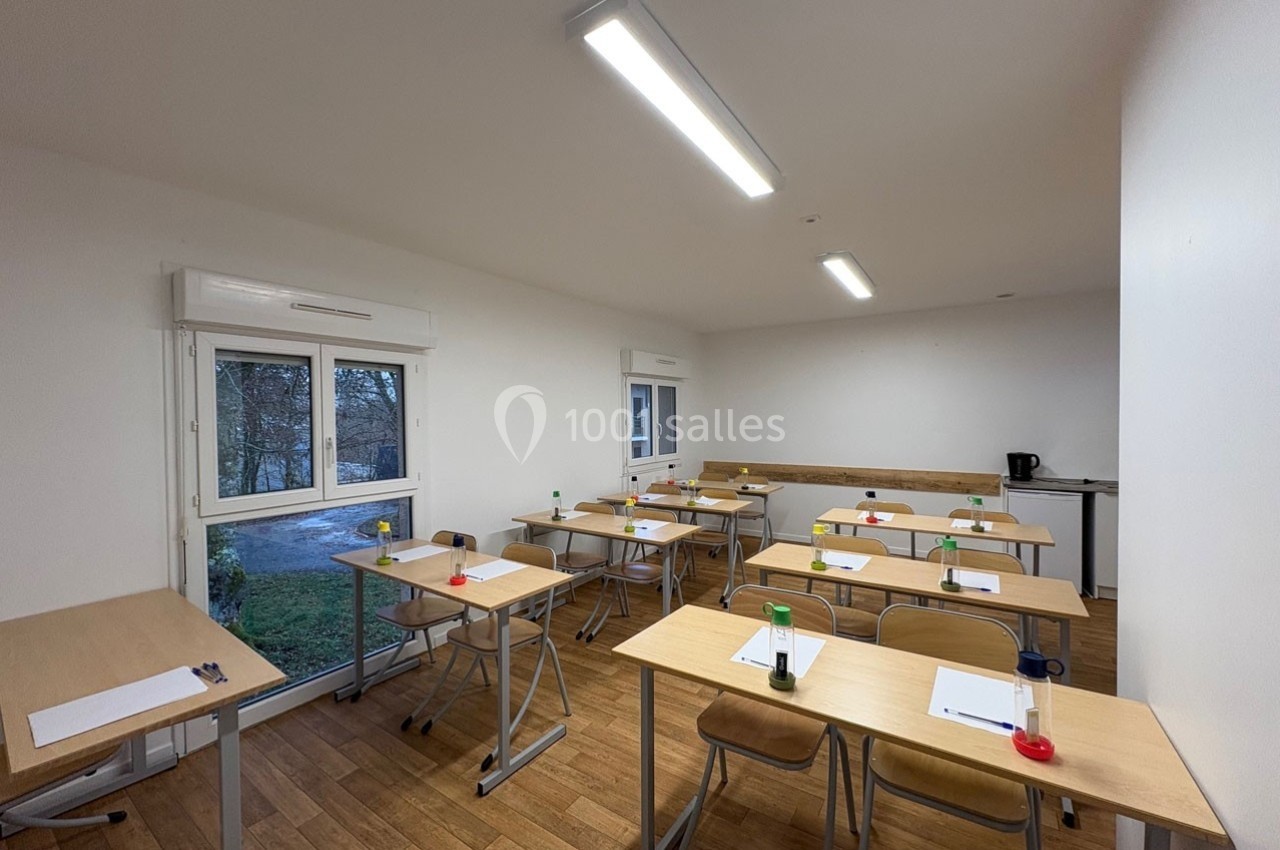 Salle de classe lumineuse avec des bureaux en bois, des chaises, des feuilles et des stylos disposés sur les tables.