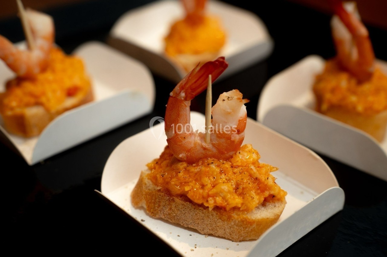 Crevettes sur des toasts garnis d'une préparation orange, présentés dans des coupelles en carton blanc.