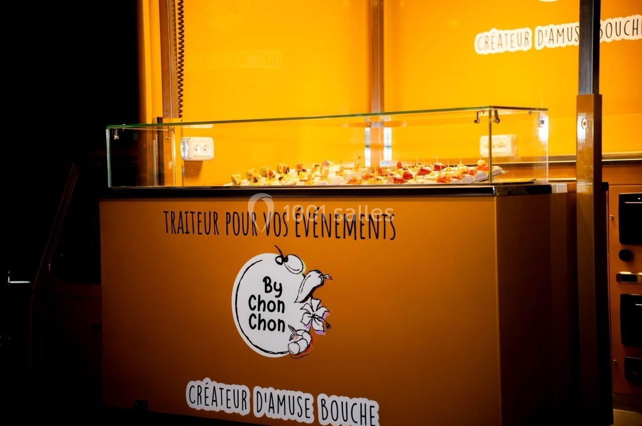 Vitrine éclairée d'un traiteur avec des amuse-bouches présentés sur un comptoir en verre, fond orange vif.