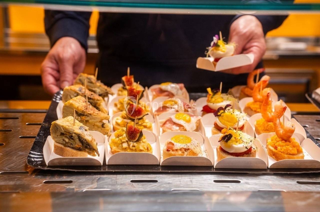 Assortiment de tapas variés présentés sur un comptoir, avec des mains ajustant les plats.