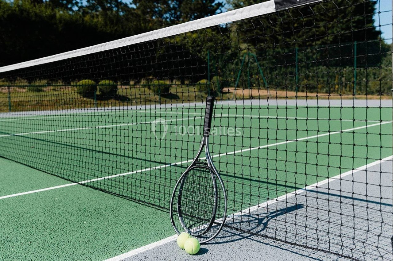 Raquette de tennis appuyée contre un filet sur un court extérieur avec une balle au sol.