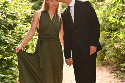 Un homme souriant tenant un appareil photo sur un chemin bordé d'arbres.