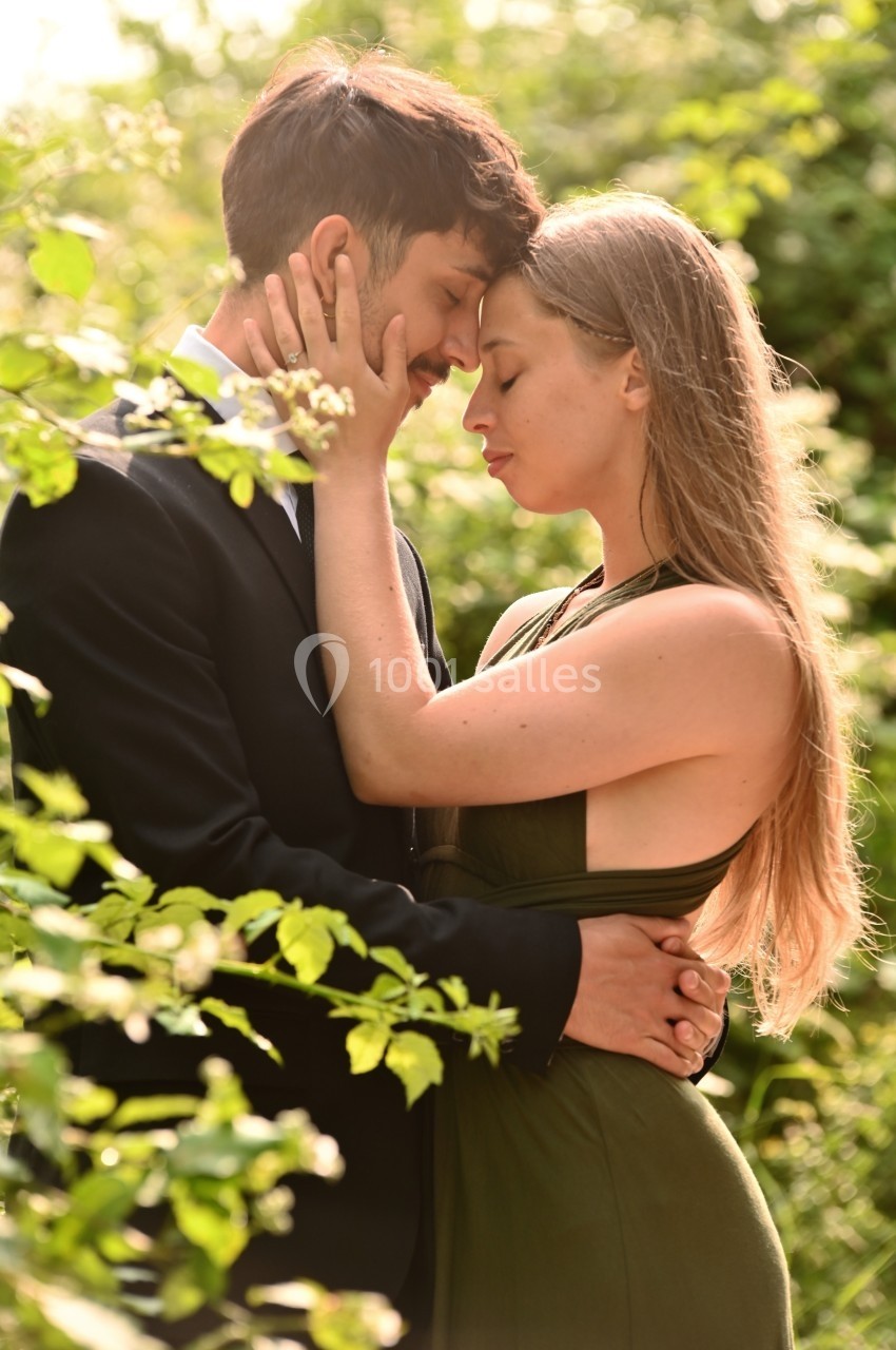 Un couple s'enlace tendrement dans un jardin verdoyant, baigné par une lumière douce.