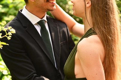 Un homme souriant tenant un appareil photo sur un chemin bordé d'arbres.