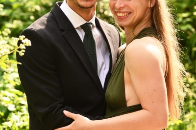 Un homme souriant tenant un appareil photo sur un chemin bordé d'arbres.