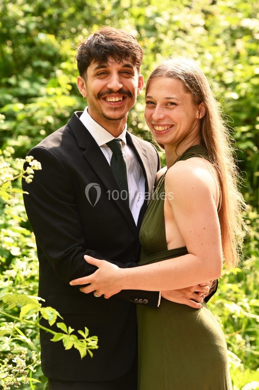 Un homme en costume et une femme en robe verte sourient ensemble dans un cadre naturel verdoyant.