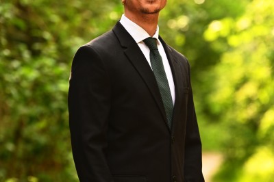 Un homme souriant tenant un appareil photo sur un chemin bordé d'arbres.