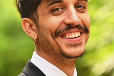 Un homme souriant tenant un appareil photo sur un chemin bordé d'arbres.