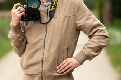 Un homme souriant tenant un appareil photo sur un chemin bordé d'arbres.