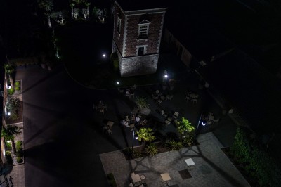 Vue aérienne d'une cour avec une tour en briques, des bâtiments anciens, des palmiers et des personnes réunies.