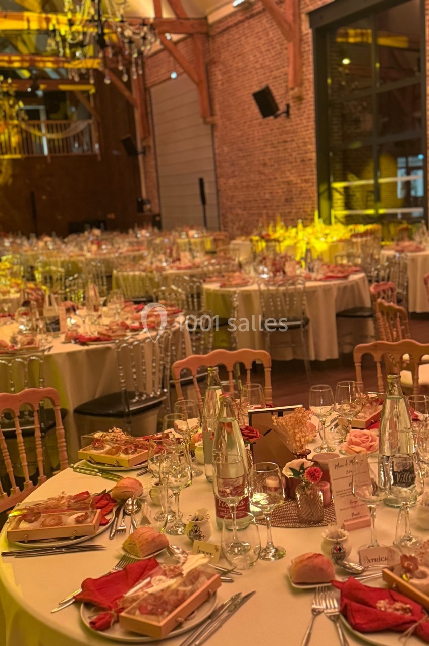 Salle de réception décorée avec des tables rondes dressées pour un événement, éclairage chaleureux et ambiance festive.