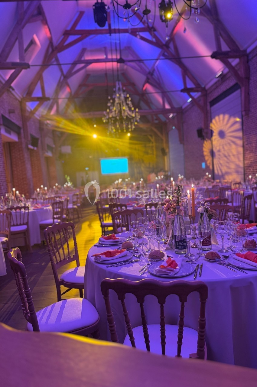 Salle de réception décorée avec des tables dressées, éclairage coloré et ambiance festive.
