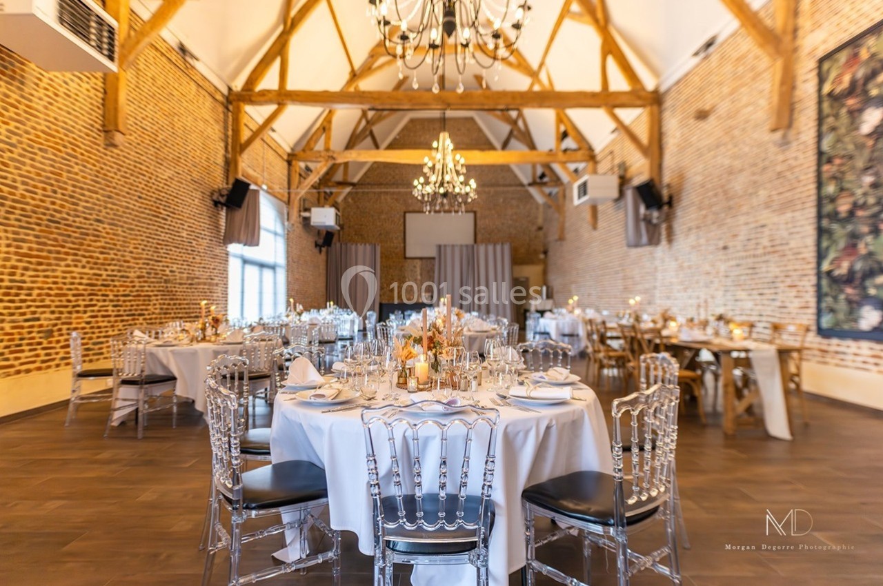 Salle de réception lumineuse avec murs en briques, poutres apparentes, tables rondes dressées et lustres suspendus.