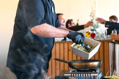 Un DJ mixe en extérieur, portant un casque audio et des lunettes de soleil, avec un mur de briques en arrière-plan.