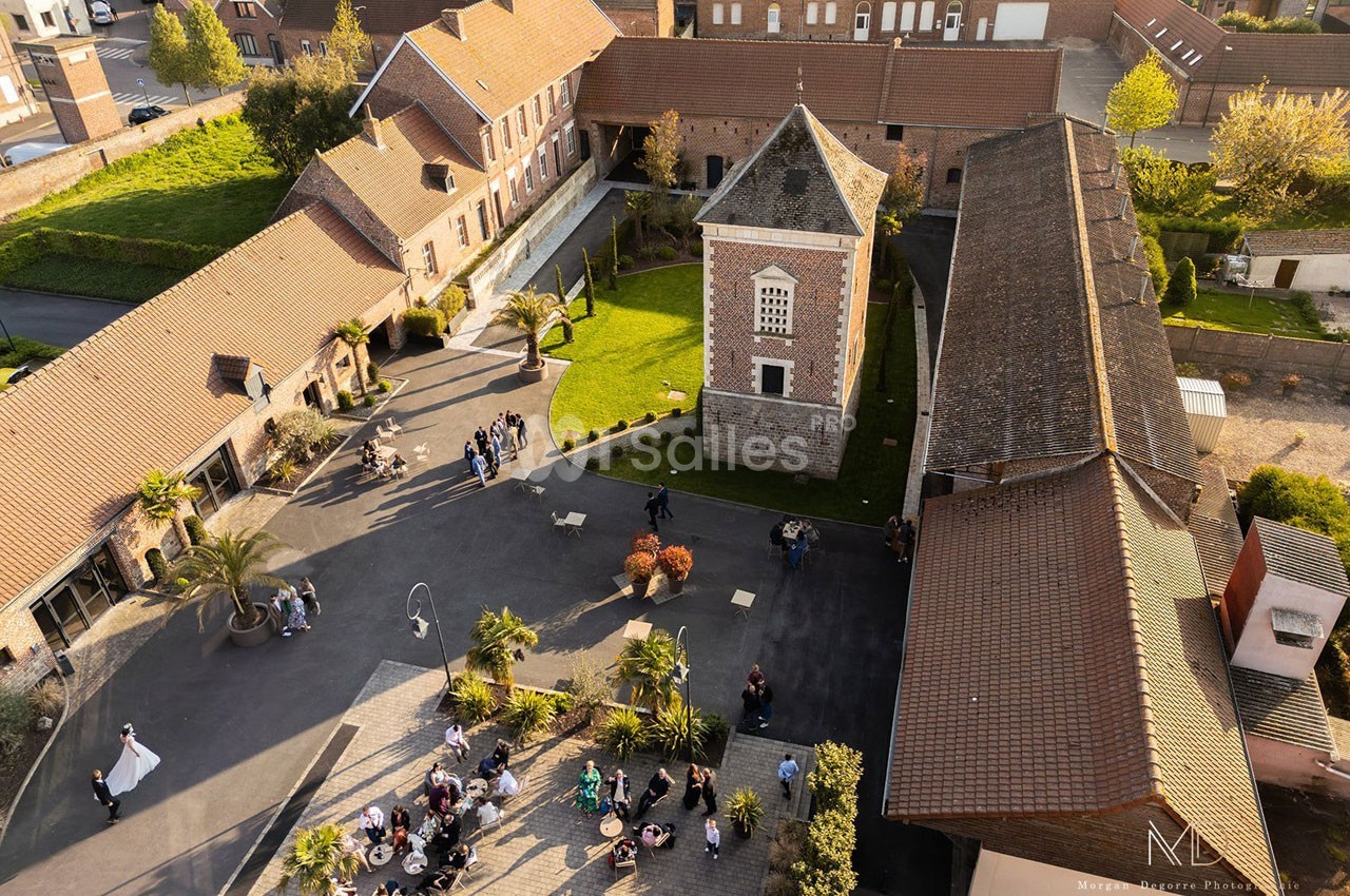 Vue aérienne d'une cour pavée entourée de bâtiments en briques, avec des groupes de personnes rassemblées.