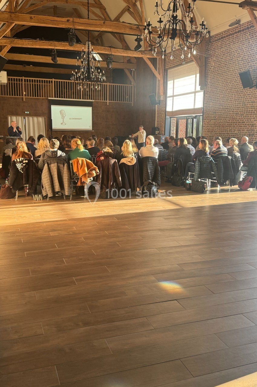 Un groupe de personnes assises dans une salle en bois avec un écran de présentation et un intervenant debout.