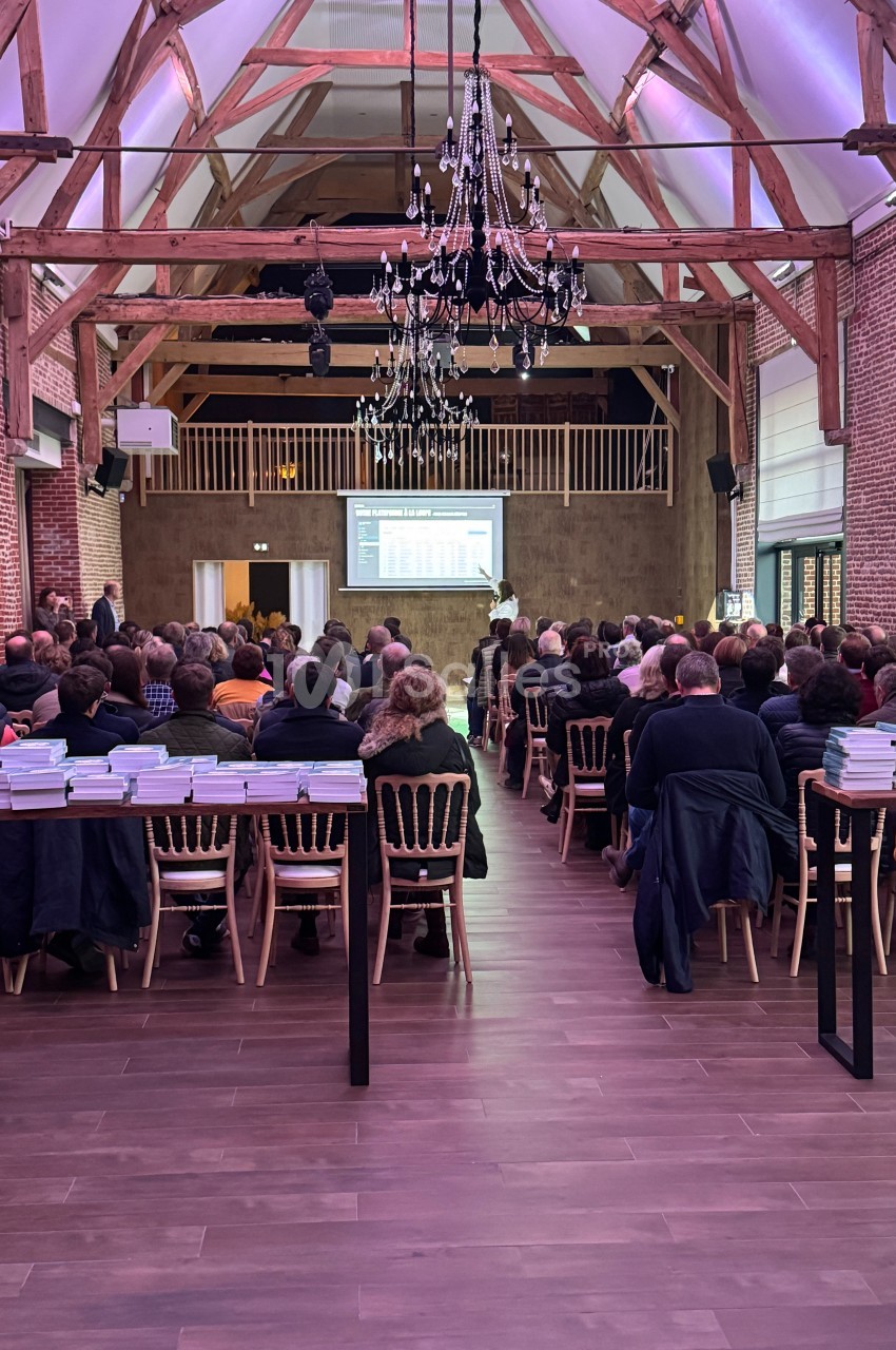 Salle comble avec des personnes assises face à un écran de présentation dans un espace à charpente apparente.
