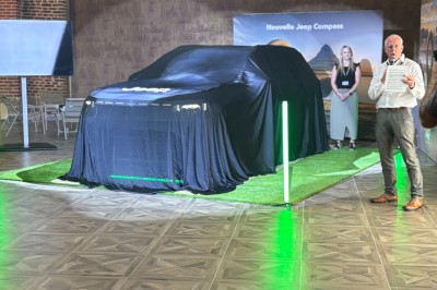 Miniature Location salle Cantin (Nord) - Le Clos du Colombier #21 SUV vert exposé dans une salle avec parquet et murs en bois, accompagné de panneaux promotionnels en arrière-plan.